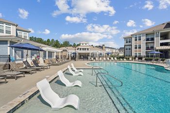 A pool with chairs around it and apartment buildings in the background.